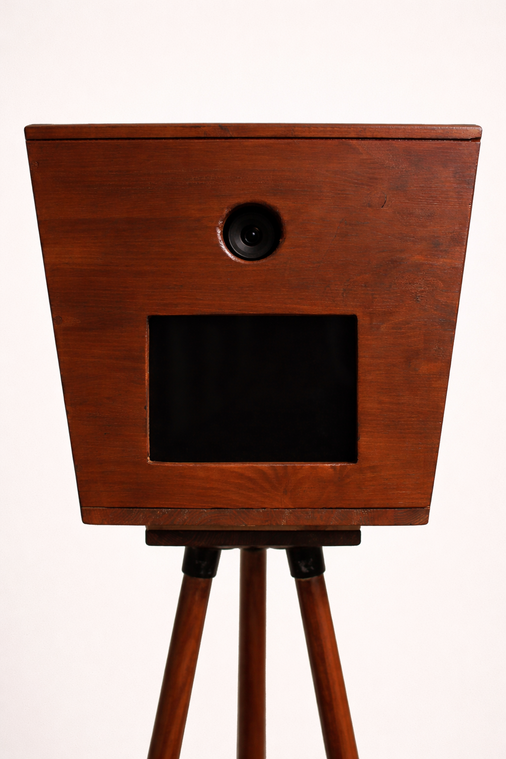 De Luxo Photobooth van Luxo heeft een cameralens boven een zwart rechthoekig scherm op een houten statief, tegen een lichte achtergrond - ideaal voor bruiloften of speciale evenementen.